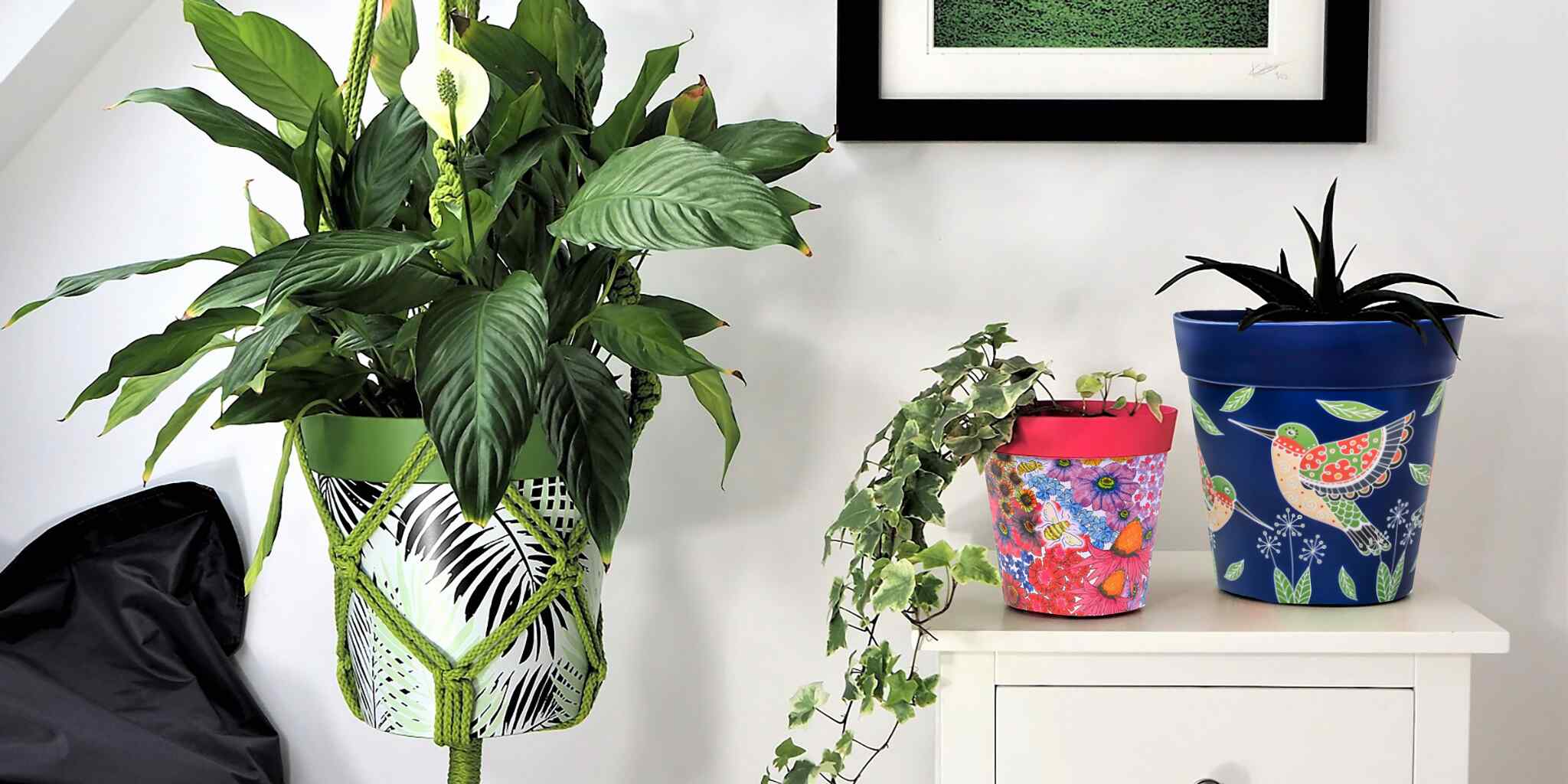 An image showing 3 Hum Flowerpots in green blue and pink floral botanical and bird patterns, one is in a macrame pot hanger